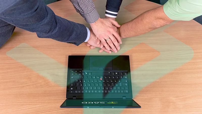 Mehrere Hände liegen als Zeichen des Teamgeists übereinander auf einem Tisch neben einem Laptop.