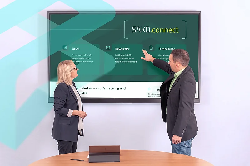 Zwei Mitarbeitende stehen vor einem Bildschirm mit SAKD.connect und den Bereichen News, Newsletter und Fachbeiträge.